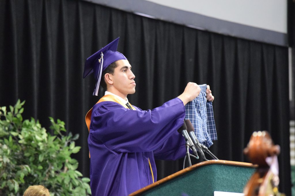 Basil Baccouche wearing a cap and gown standing at a podium holding a pair of boxer shorts.