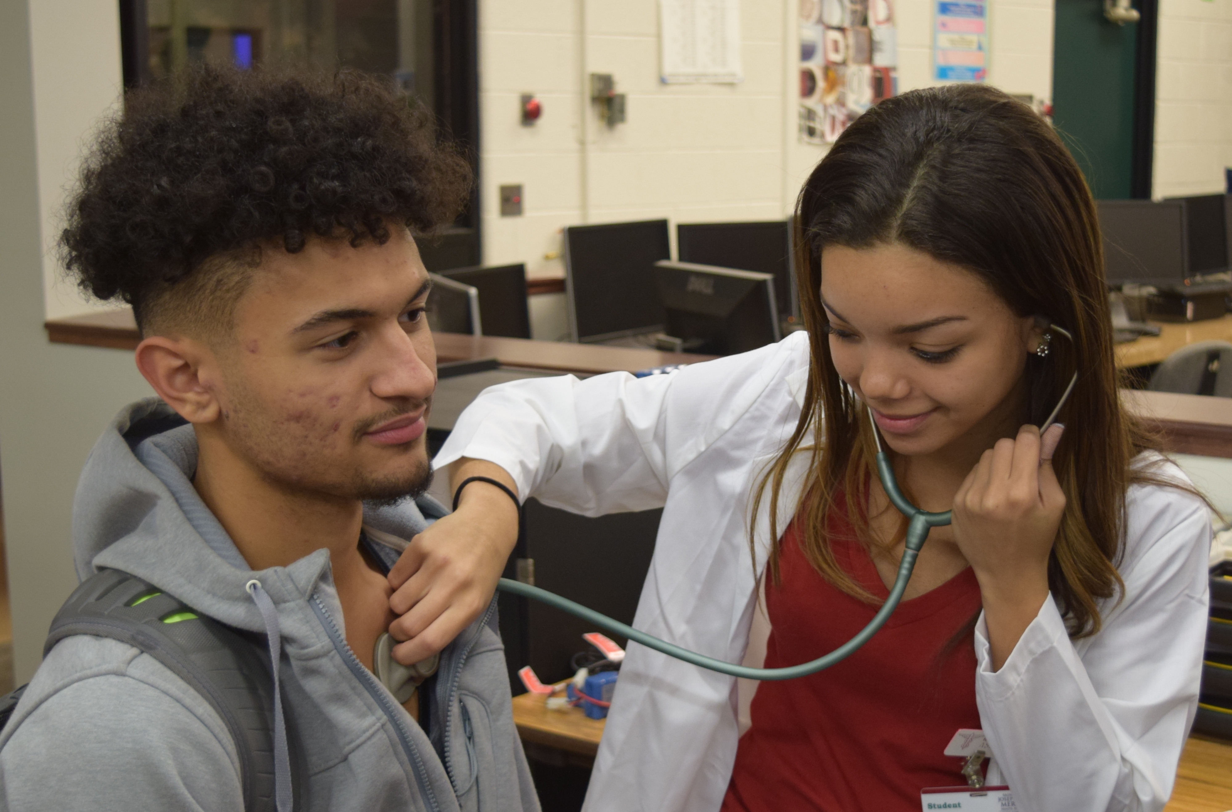 A female student with a stethoscope checks the heart beat of a male student.