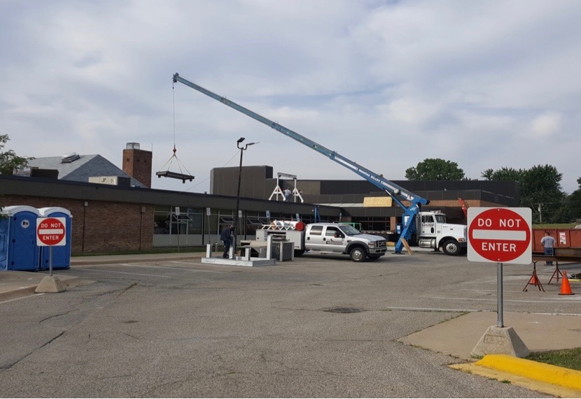 A construction crane lifting a large piece of metal onto the roof of Allen Elementary School