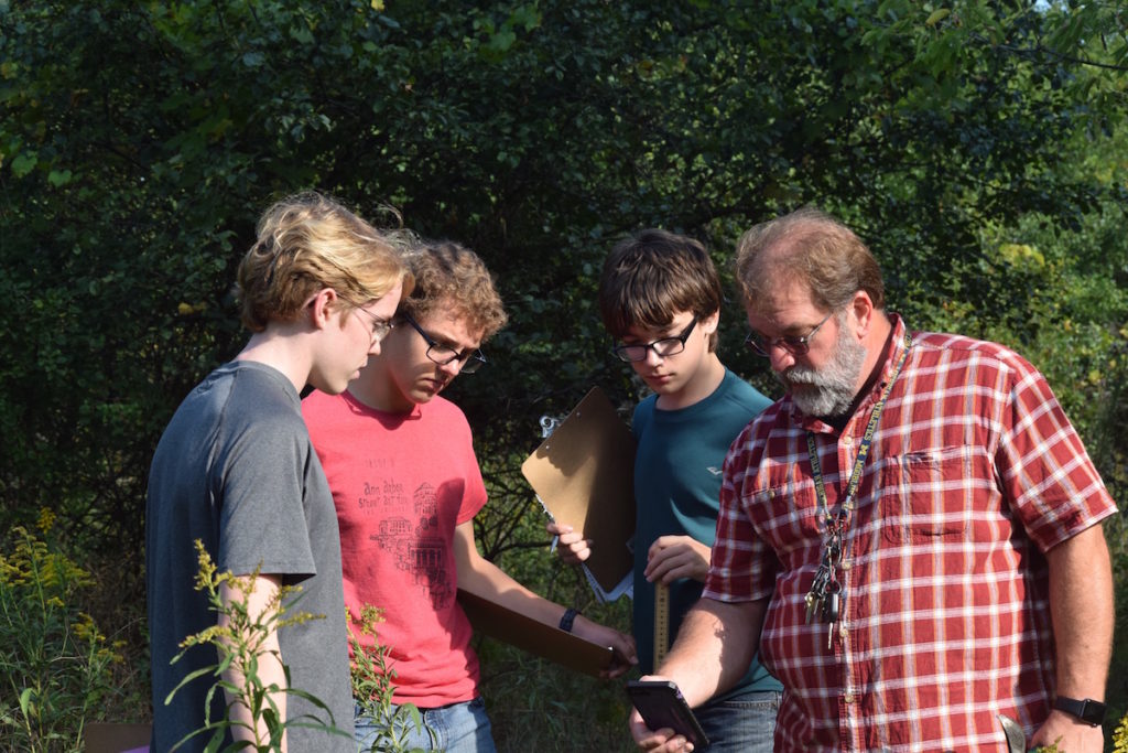 3 male Skyline students and Environmental Education Consultant Dave Szczygiel look at his phone to help identify a plant