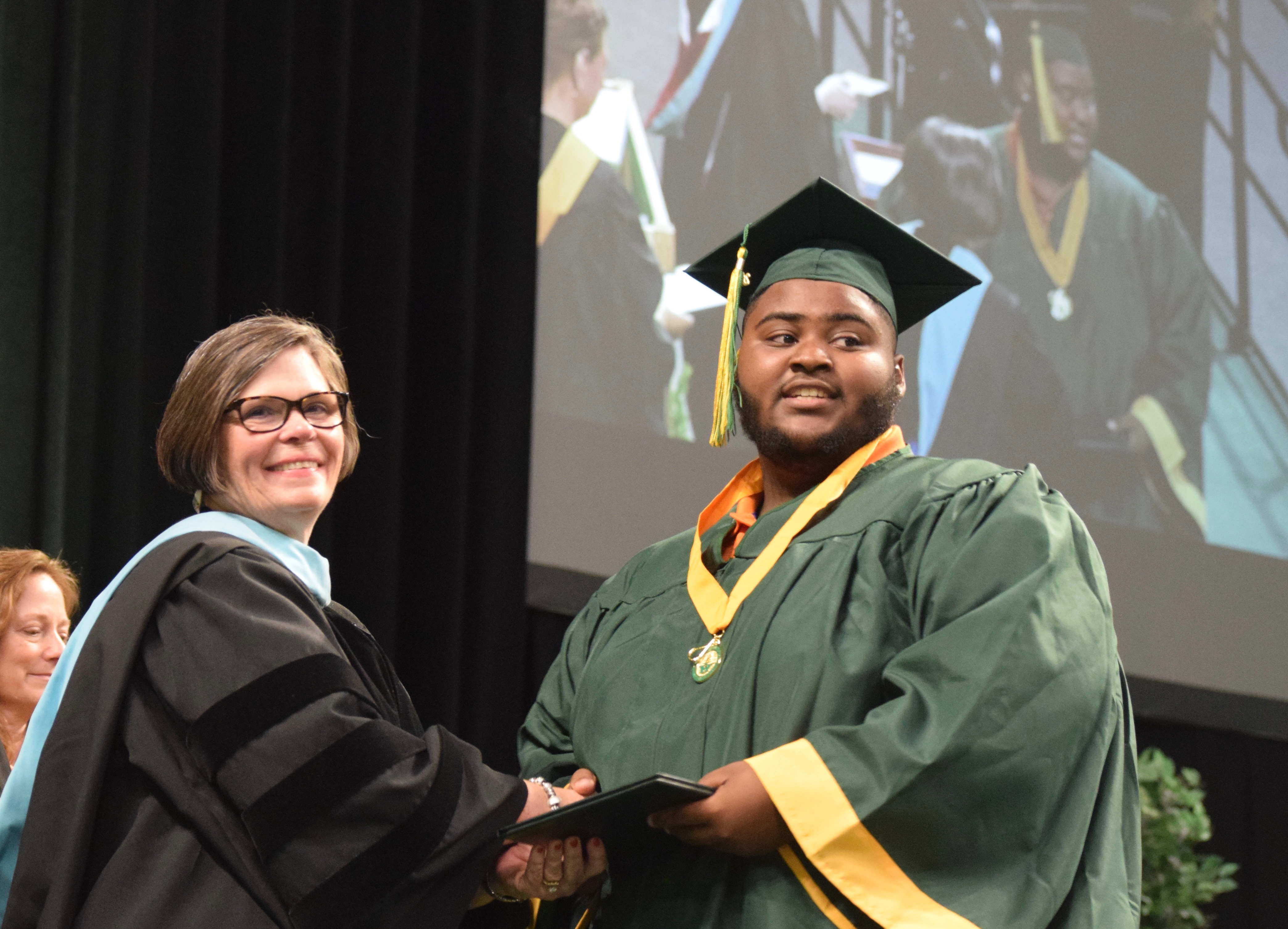 An African-American graduate and Principal Janet Schwamb smile as she hands him his diploma