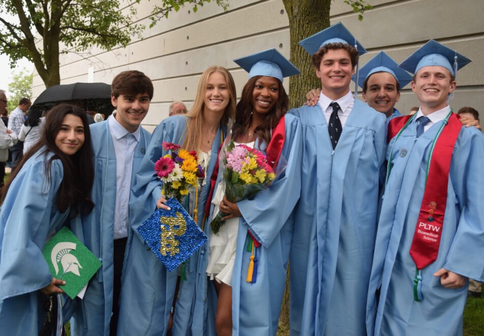 A group of Skyline students outside after the graduation ceremony, still wearing caps and gowns, several with flowers