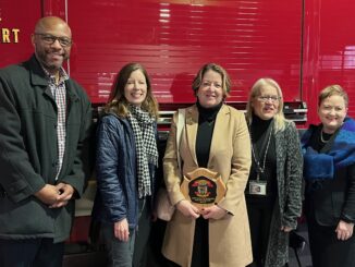 John Randle, Jenna Bacolor, Liz Margolis, Hanna Melangton, and Jeanice Swift stand in front of a fire truck as Margolis holds a plaque honoring her for emergency preparedness work.