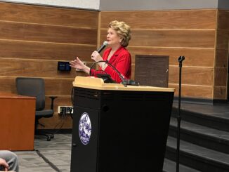 Senator Debbie Stabenow holding a microphone talking behind a lectern at Pioneer High School.
