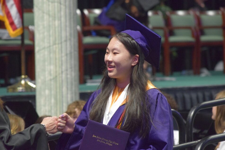 A female Pioneer student fist bumps a staff member after receiving her diploma.