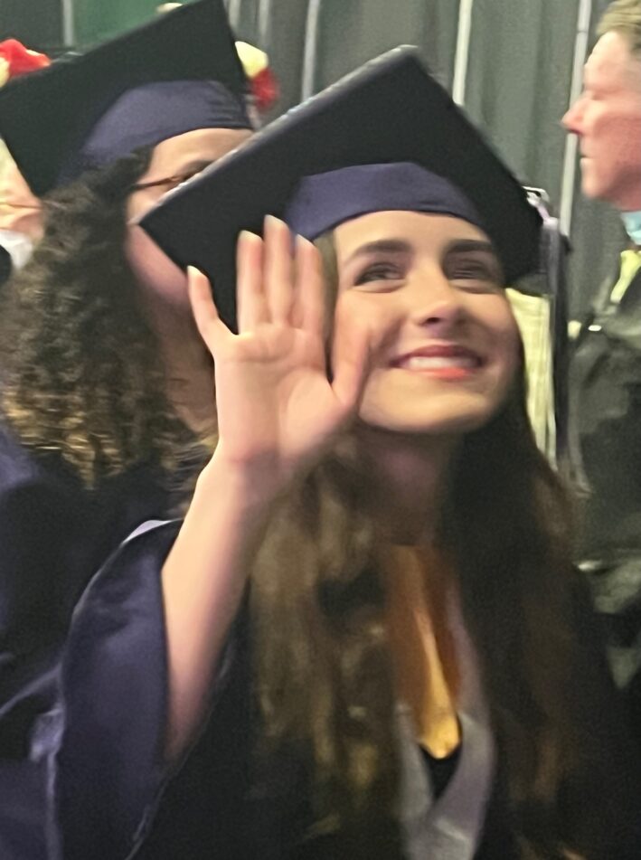 A female Pioneer student in cap and gown waves after the ceremony.