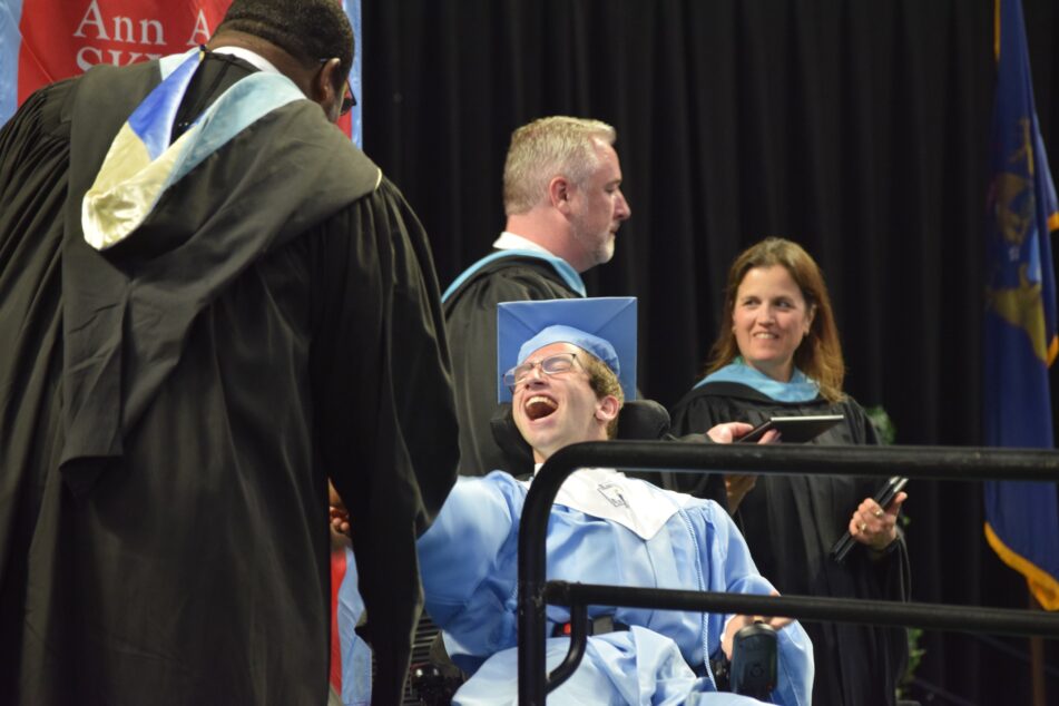 A Skyline student in cap and gown in his wheelchair receives his diploma.