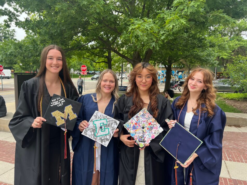 A group of four female Community grads in gowns showing their caps outside before the ceremony.