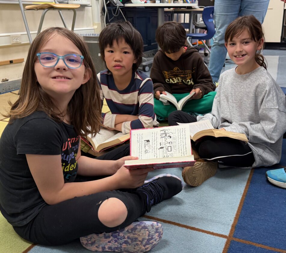 Young Angell students sitting on a rug reading in class.