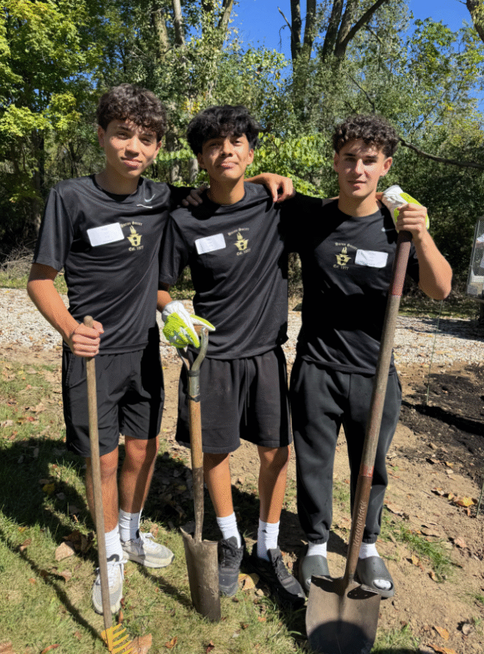 Three male Huron volunteers smile while standing with shovels