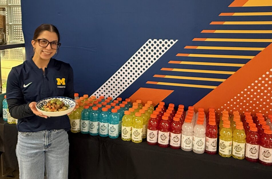 Gymnast Reyna Guggino holds a chipotle lime chicken and brown rice bowl and stands in front of a display of Gatorade Zero at Slauson