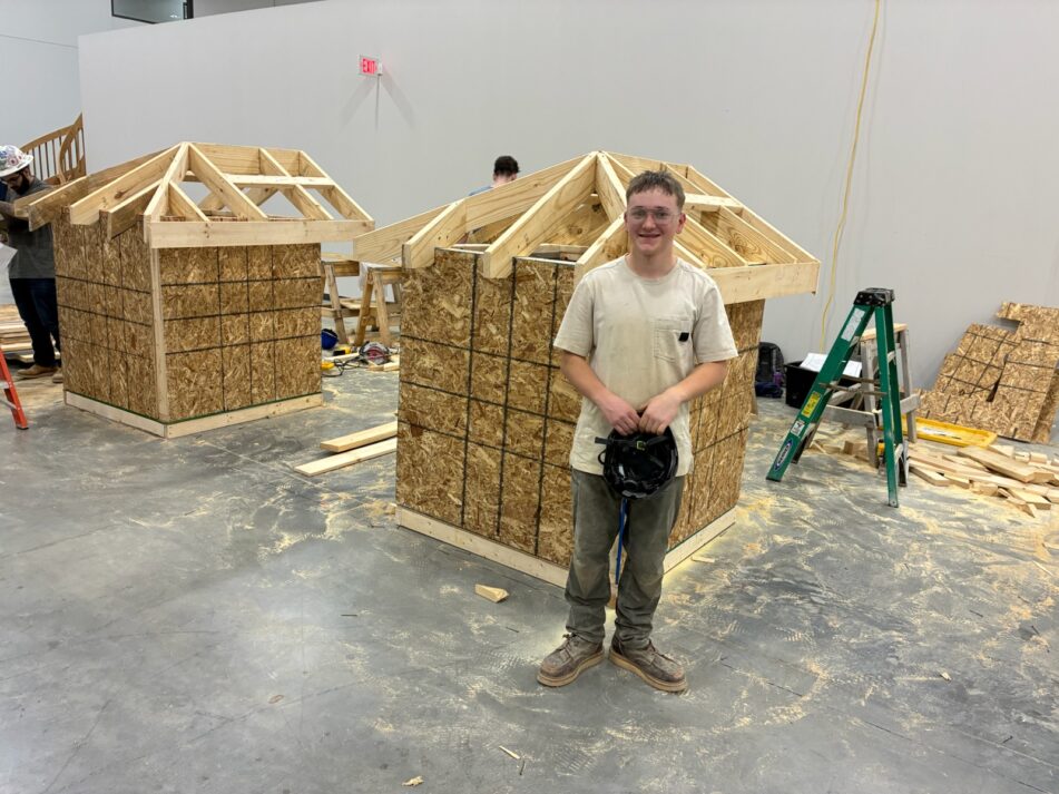 A student stands in front of the structure he built to demonstrate his homebuilding skills.