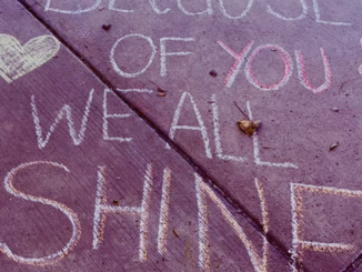 Still shot from a video honoring educators, with eh words "Because of you we all shine" written in chalk on a sidewalk