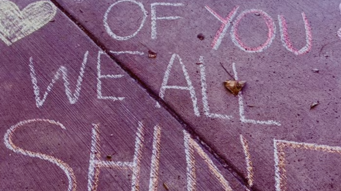Still shot from a video honoring educators, with eh words "Because of you we all shine" written in chalk on a sidewalk