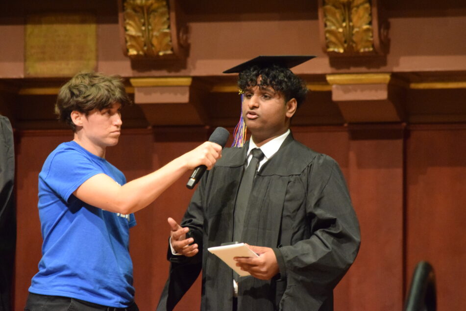 Community grad gives his speech while forum leader holds the microphone.