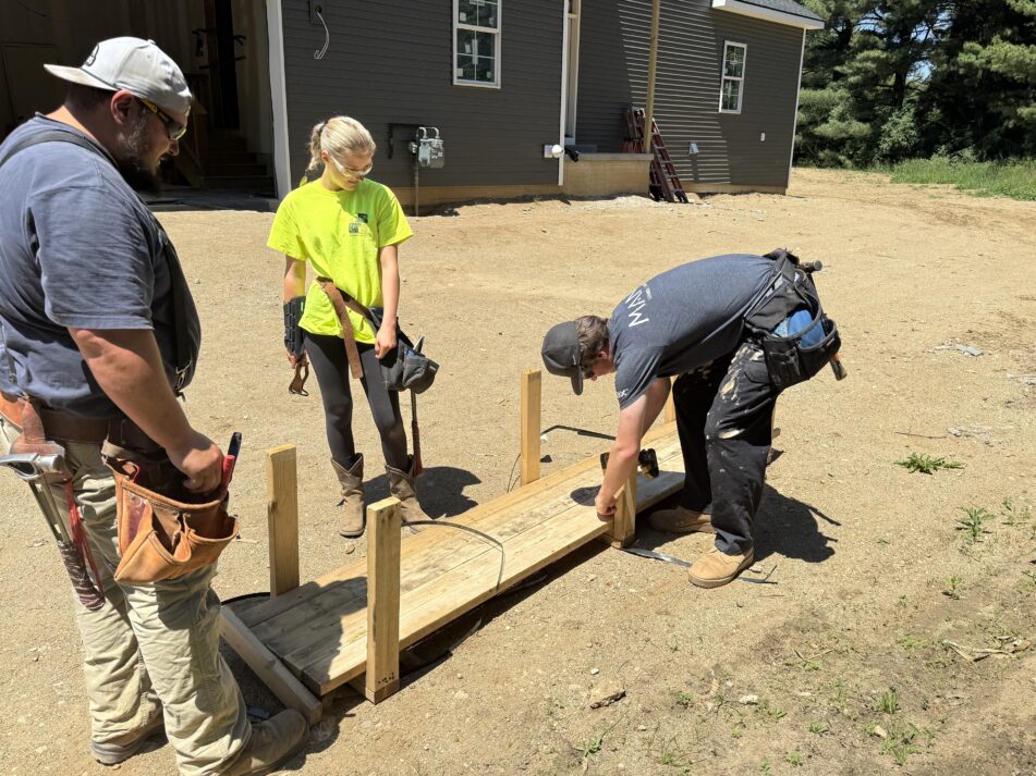 A couple of students and assistant instructor Grant Welch work outside the house.