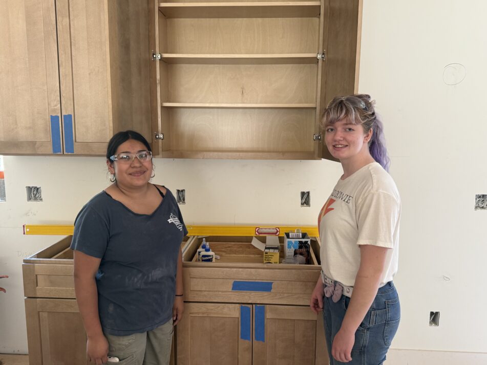 A couple of students pose next to some of the kitchen cabinets in the nearly finished house.